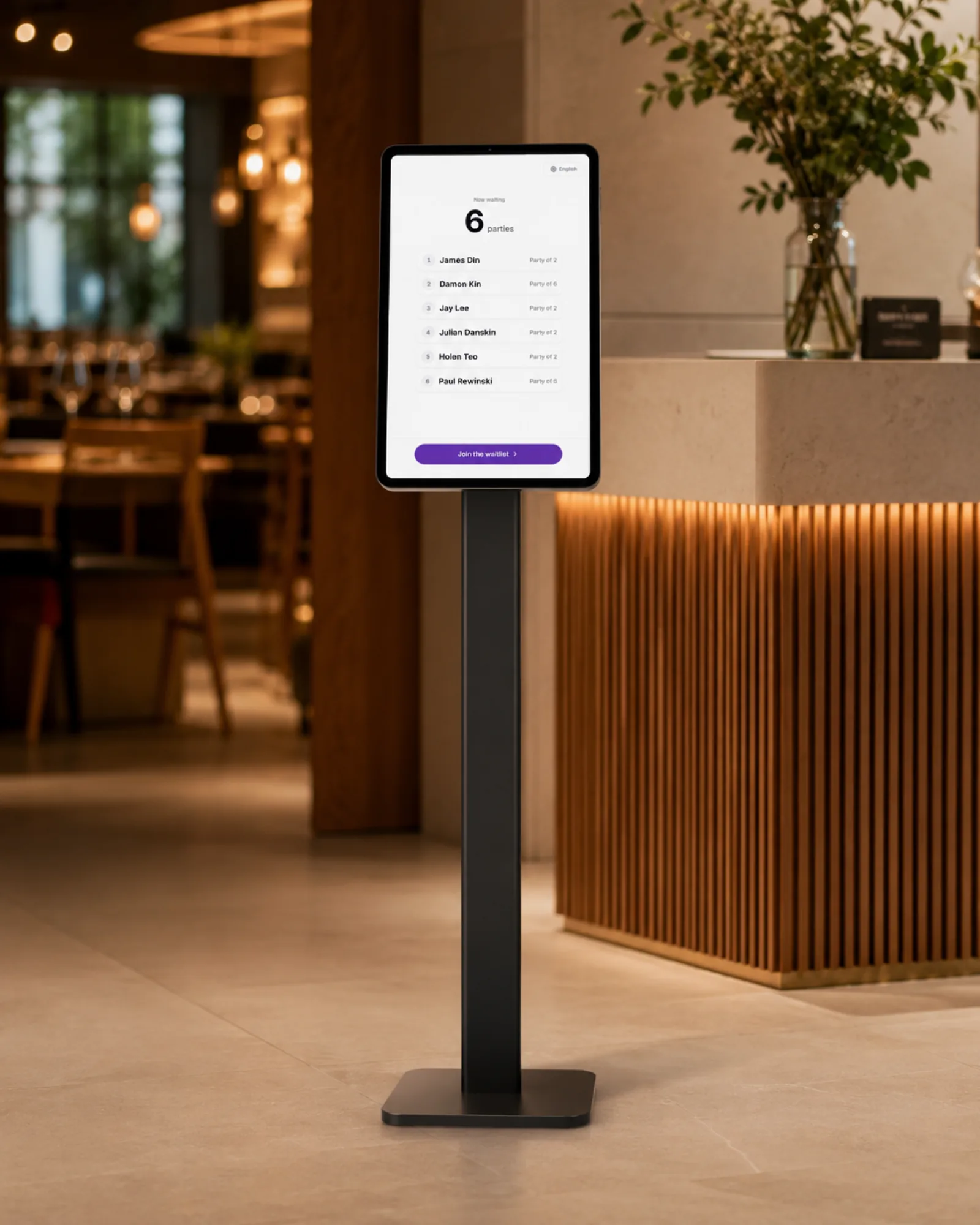 A tablet on a floor stand at a restaurant entrance showing the waitlist and a join button